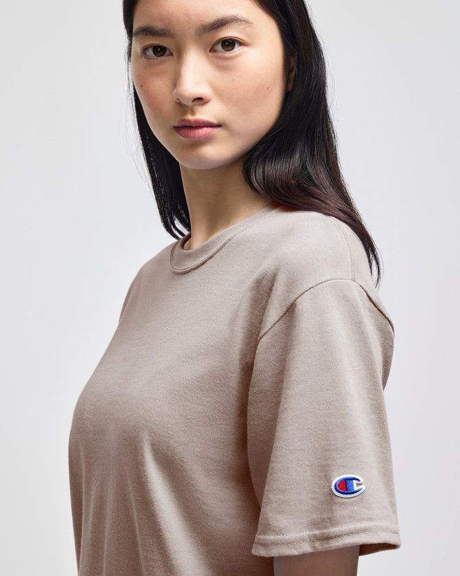 A beige Champion adult short-sleeve t-shirt featuring a logo on the left sleeve.