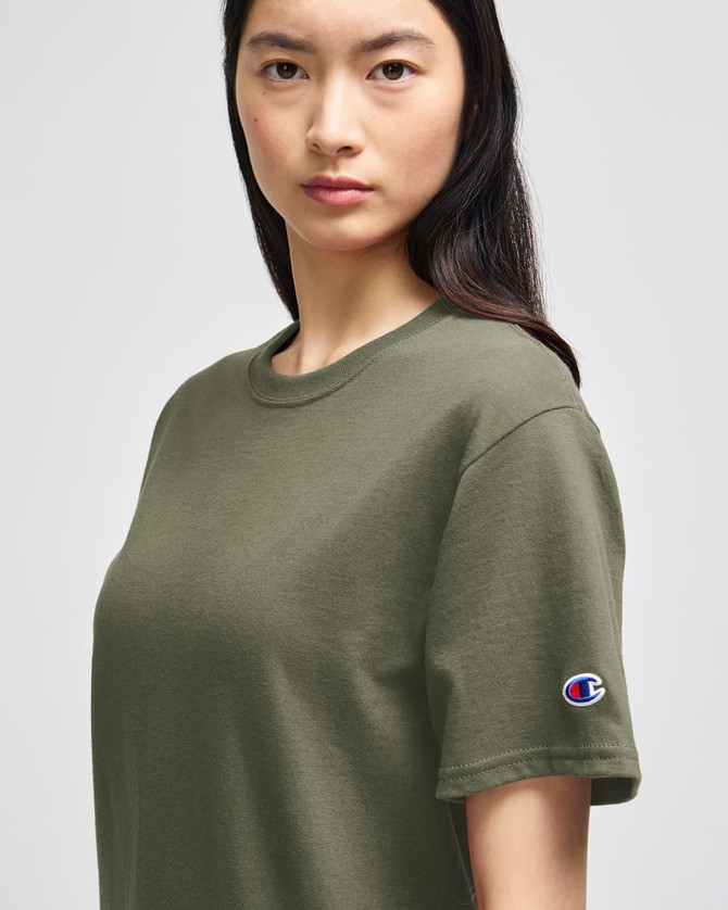 An olive green Champion adult short-sleeve t-shirt displayed on a model, featuring a small logo on the sleeve.