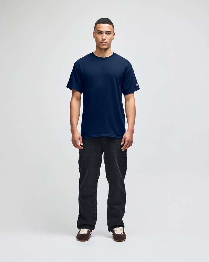 A model wearing a navy blue short-sleeve t-shirt and black pants, featuring a branding logo.