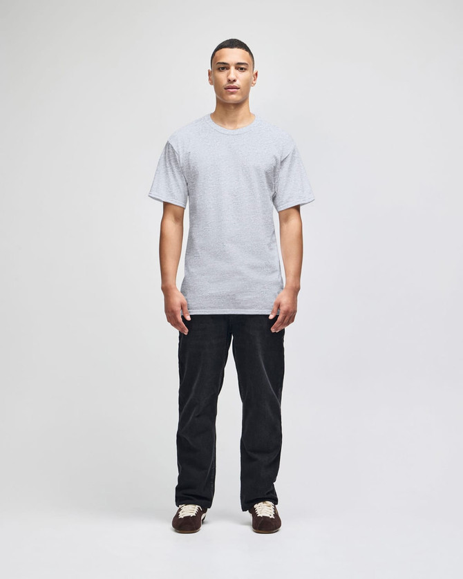 A model stands in a grey Champion adult short-sleeve T-shirt, paired with black pants. The shirt features a logo.