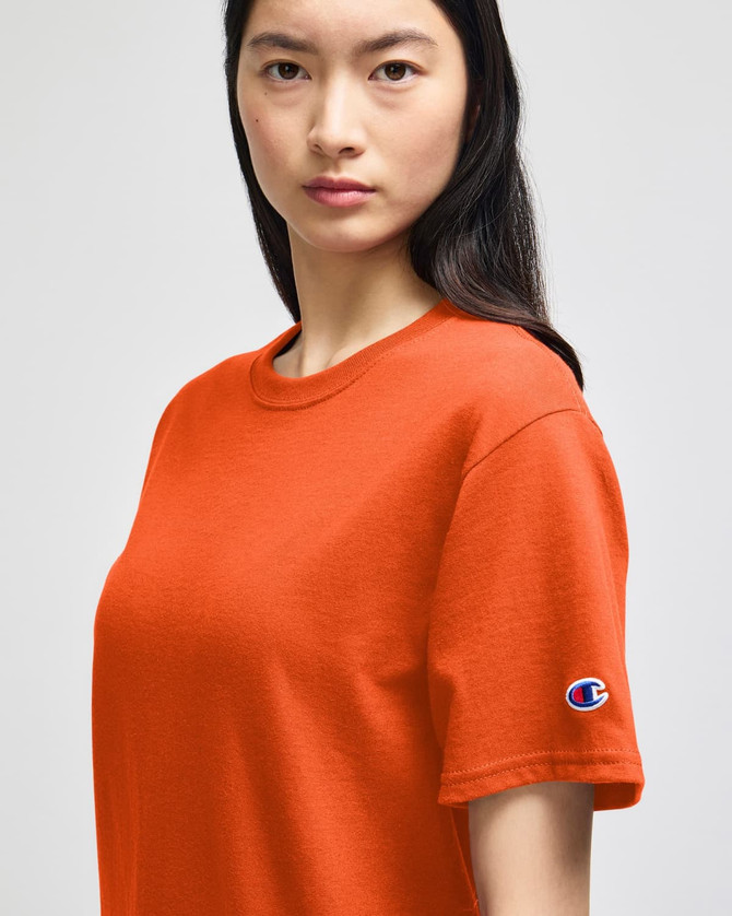 An orange Champion adult short-sleeve t-shirt, featuring a logo on the left sleeve.