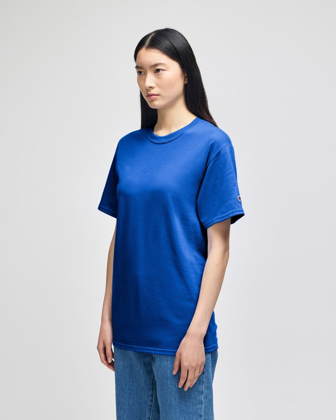 A blue Champion adult short-sleeve t-shirt with a logo, paired with blue jeans, displayed on a model.