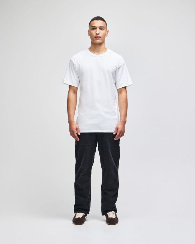 A man wearing a plain white short-sleeve t-shirt paired with black trousers; the shirt features a logo.