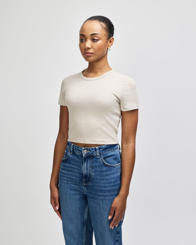 A light beige women's crop fitted T-shirt paired with blue high-waisted jeans, featuring a logo.