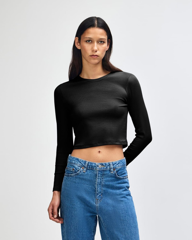 A black long-sleeve crop fitted t-shirt on a model, paired with blue jeans. The shirt features a logo.