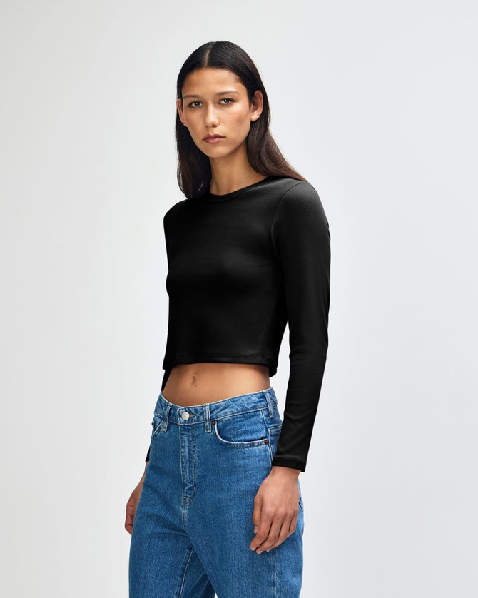 A black long-sleeve cropped fitted t-shirt displayed on a model, paired with blue jeans. Features a logo.