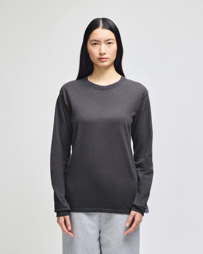 A long-sleeve t-shirt in dark grey, featuring a logo on the sleeve. Model wearing grey pants.