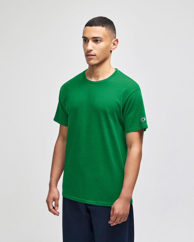 A green Champion adult jersey short sleeve t-shirt displayed on a model, featuring a logo on the sleeve.