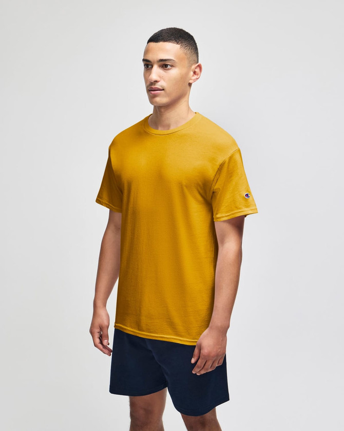 A short sleeve t-shirt in mustard yellow, featuring a logo on one sleeve, displayed on a model.