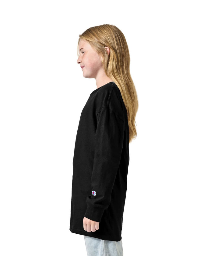 A black long sleeve youth t-shirt displayed on a model standing sideways, featuring a logo on the sleeve.