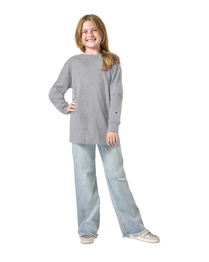 A grey long sleeve T-shirt is worn by a girl standing with her hands on her hips, paired with light blue jeans.