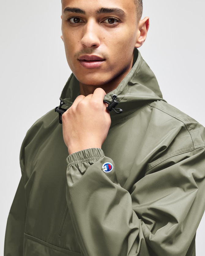 A man wearing a green Champion packable anorak jacket with a hood, featuring a logo on the sleeve.