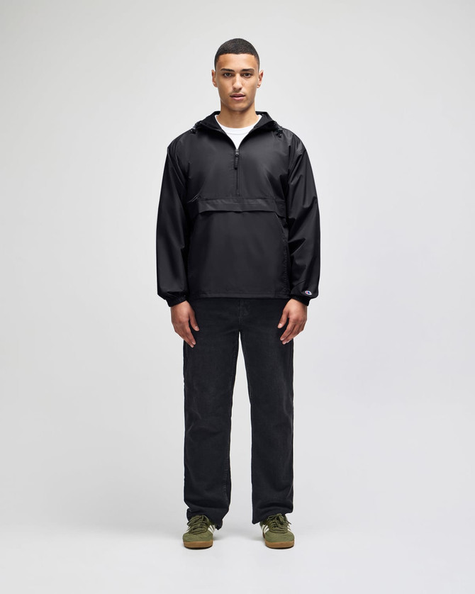 A black packable anorak jacket worn by a model, paired with dark trousers and shoes, featuring a logo.