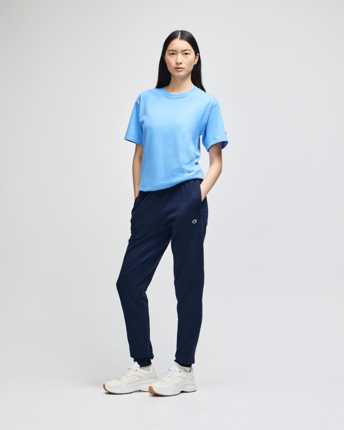 A model wearing navy fleece joggers paired with a light blue t-shirt and white sneakers, featuring a logo.