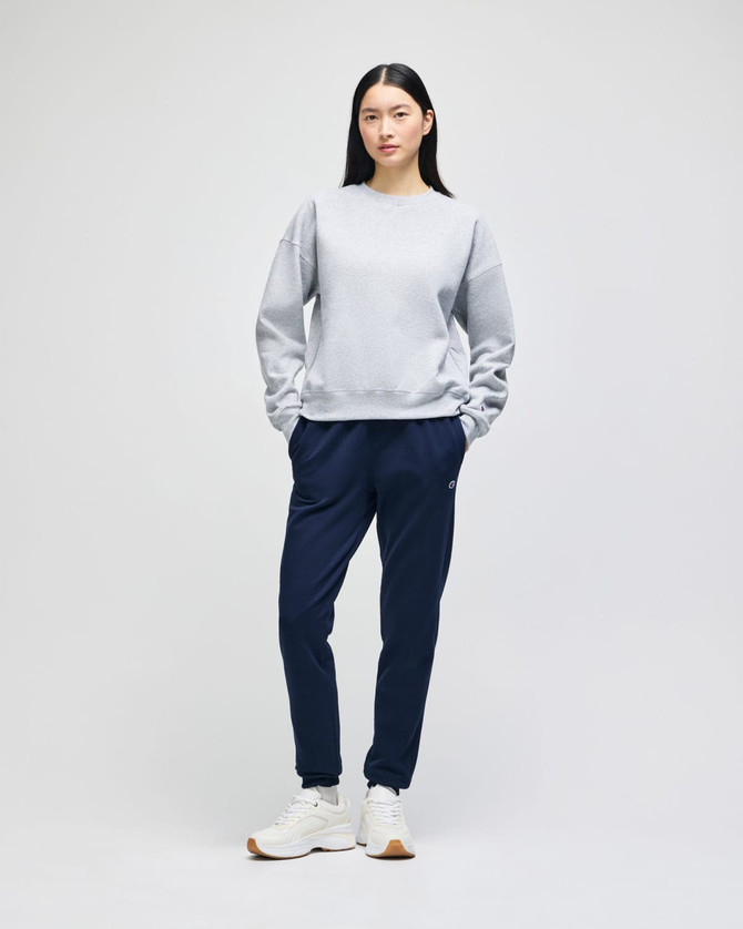 A grey women's crewneck sweatshirt paired with navy sweatpants and white sneakers, featuring a logo.