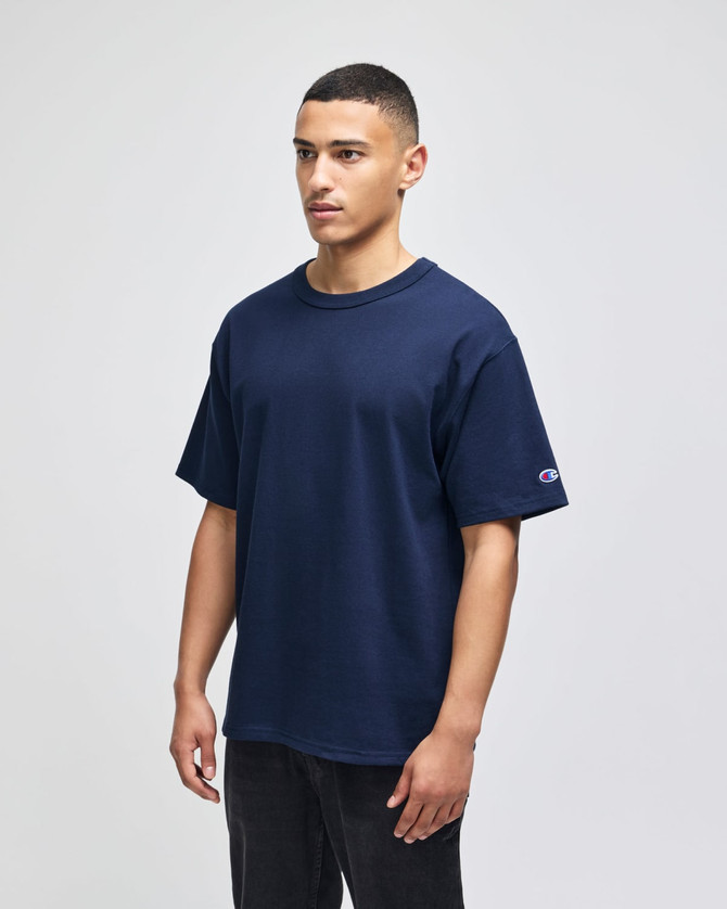 A navy blue Champion Adult Heritage Jersey T-Shirt displayed on a model. The shirt features a logo on the sleeve.