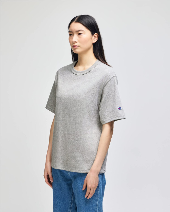 A grey Champion Adult Heritage Jersey T-Shirt displayed on a model, featuring a logo on the sleeve.