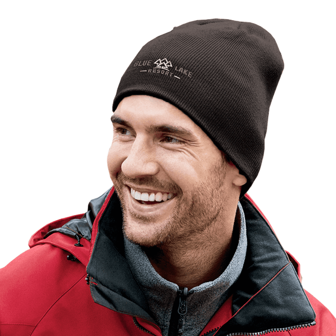 A man wearing a brown knitted beanie smiles, paired with a red jacket and grey sweater, featuring a logo on the beanie.