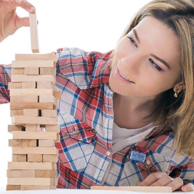A woman stacking wooden blocks in a game of Tumbling Tower, featuring light-coloured natural wood blocks.