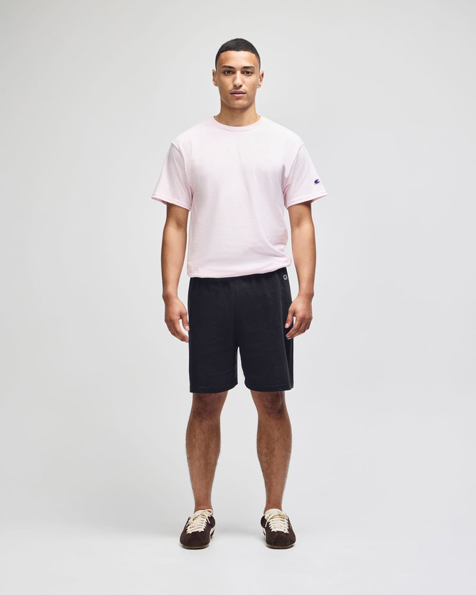 A man wearing a pink t-shirt and black cotton gym shorts, featuring a logo on the shorts.