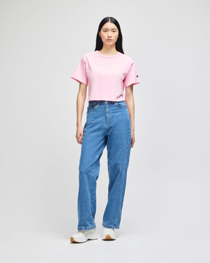 A cropped short sleeve t-shirt in pink, paired with high-waisted blue jeans, showcased on a model.