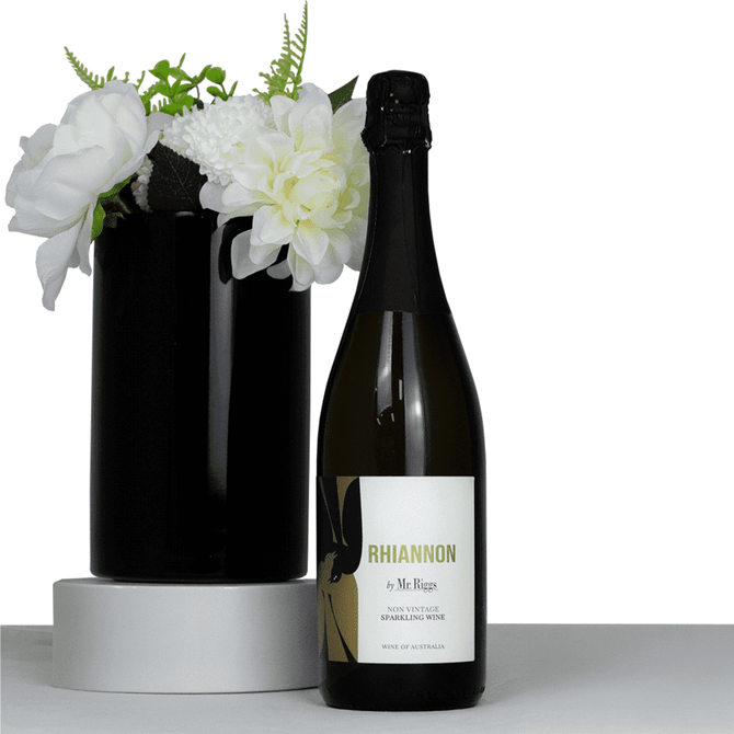 A sparkling wine bottle with a black label next to a black vase filled with white flowers.