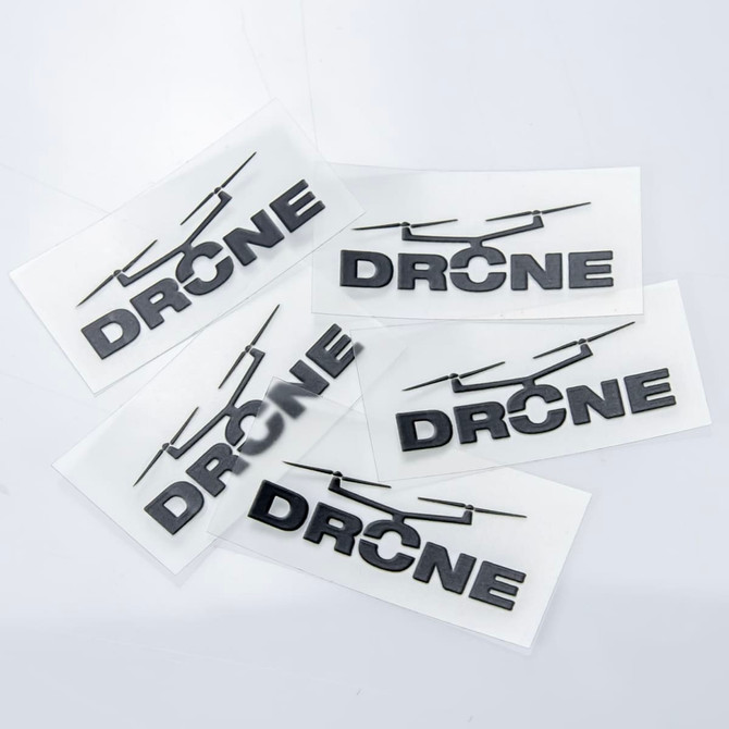 Four black "DRONE" stickers on a clear backing, arranged on a light grey surface.