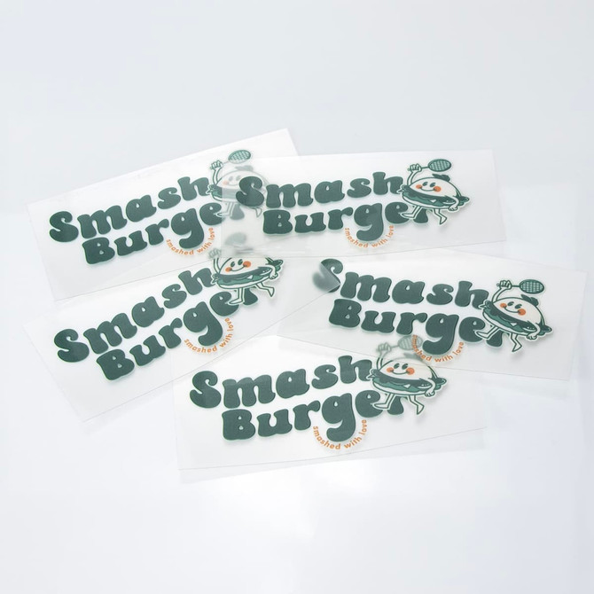 A collection of green and white stickers featuring a playful logo and branding for "Smash Burger."