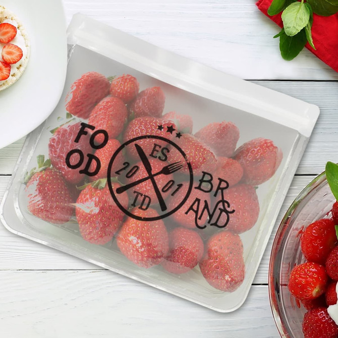 A transparent reusable pouch filled with fresh strawberries, featuring a circular logo design.