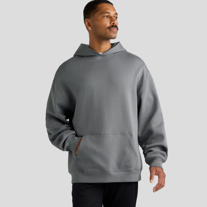 A grey hoodie with a kangaroo pocket and a hood, worn by a man standing against a plain background.