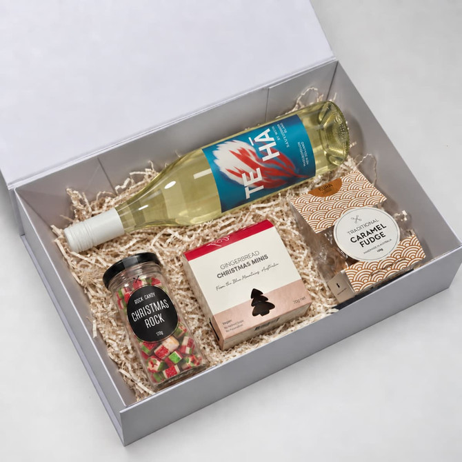 A drink bottle of white wine, a jar of Christmas rock, a box of Christmas snacks, and a pack of caramel fudge in a gift box.