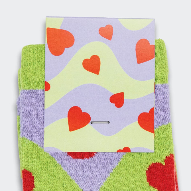 Bright green and purple knitted socks featuring a heart pattern, with a card displaying a similar design.