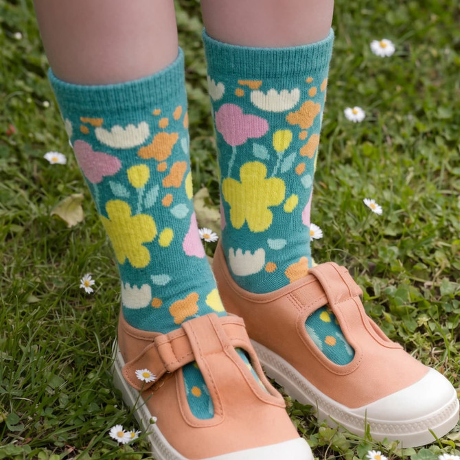 Jolly knitted bamboo kids' socks in teal with colourful floral patterns, worn with light-coloured shoes on grass.