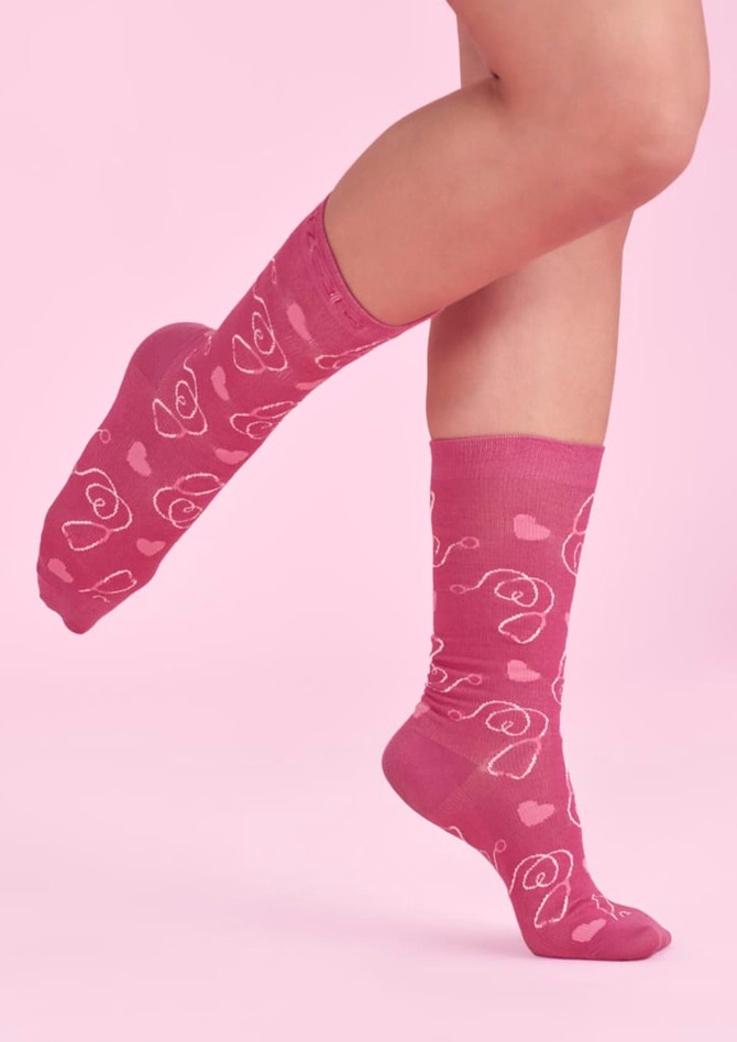 Unisex pink socks featuring a playful heart and flower design, displayed on a foot against a pink background.