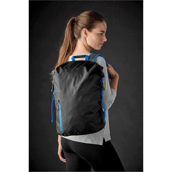 A black backpack with blue zippers, worn on the back of a model against a dark background.