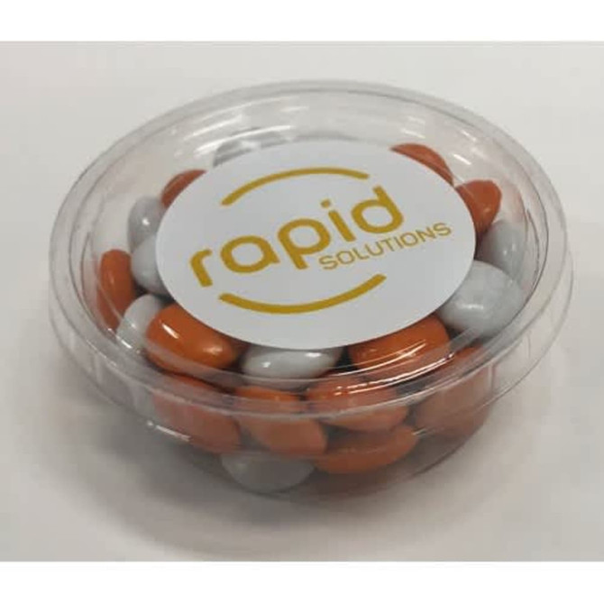 A clear tub filled with orange and grey choc beans, featuring a circular logo on the lid.