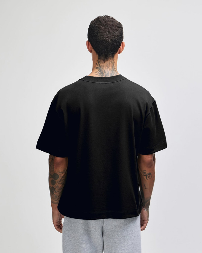 A black heavyweight cotton unisex boxy T-shirt displayed from the back, worn over grey shorts.