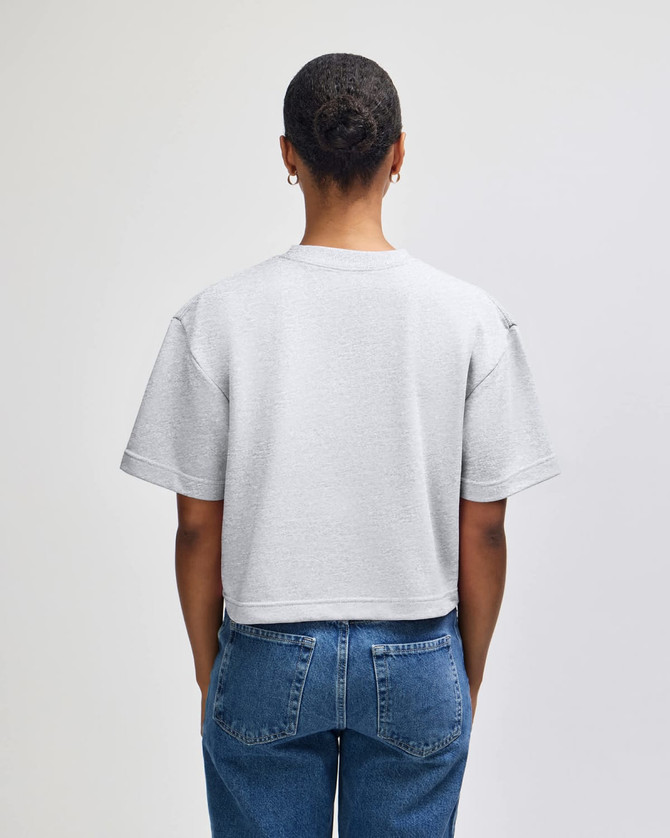 A mid-length, boxy women's top in grey, featuring short sleeves and a relaxed fit. It has a logo on the back.