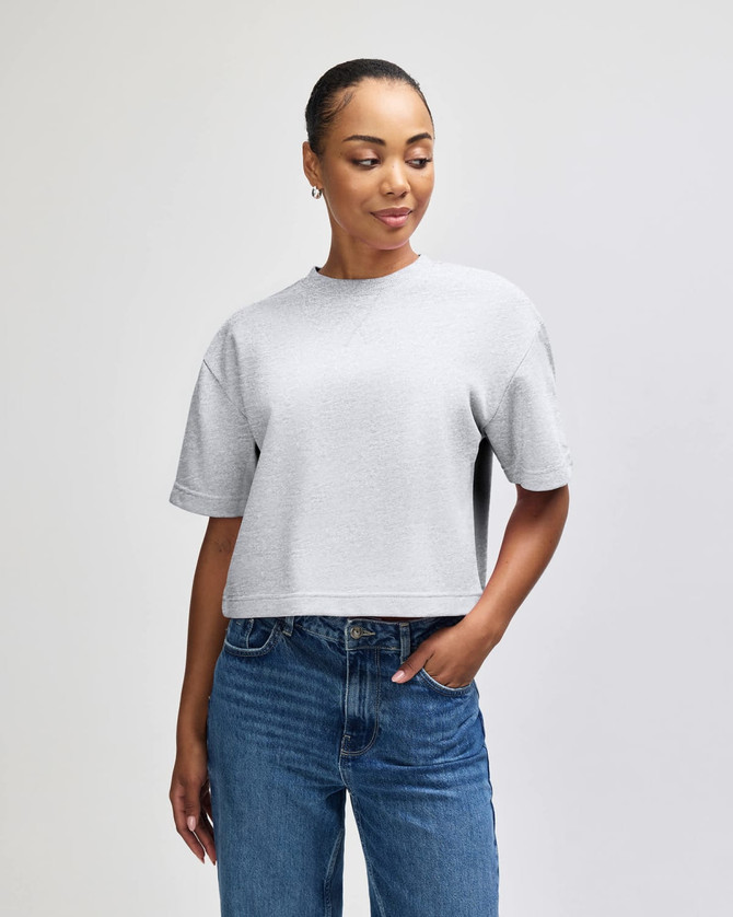 A grey women's mid-length boxy top with short sleeves, featuring a relaxed fit and a brand logo.