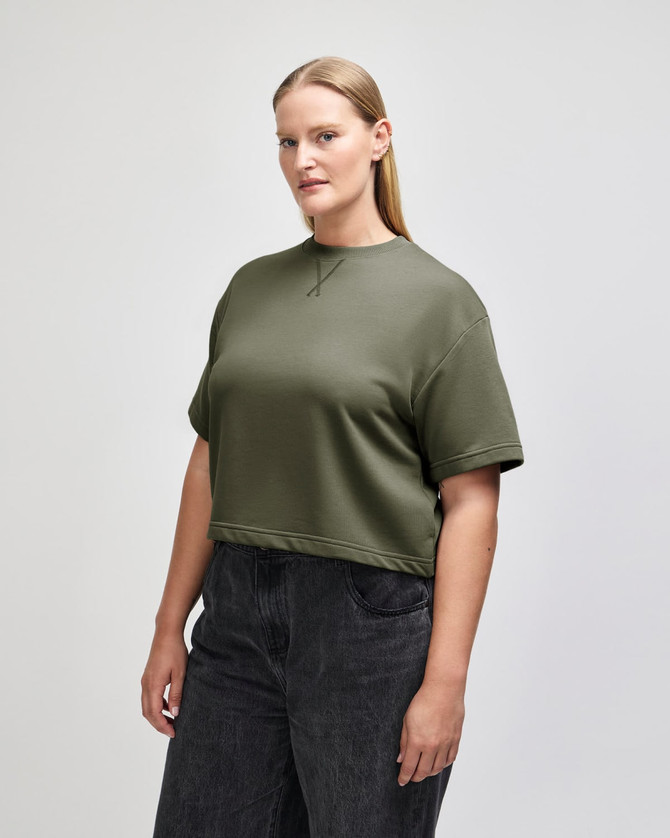 A women's mid-length boxy top in olive green, featuring short sleeves and a relaxed fit, with a logo.