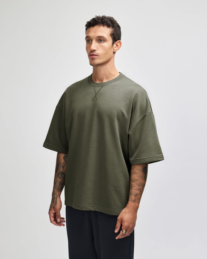 A unisex oversized boxy top in olive green, featuring short sleeves and a casual fit. The shirt has a logo.
