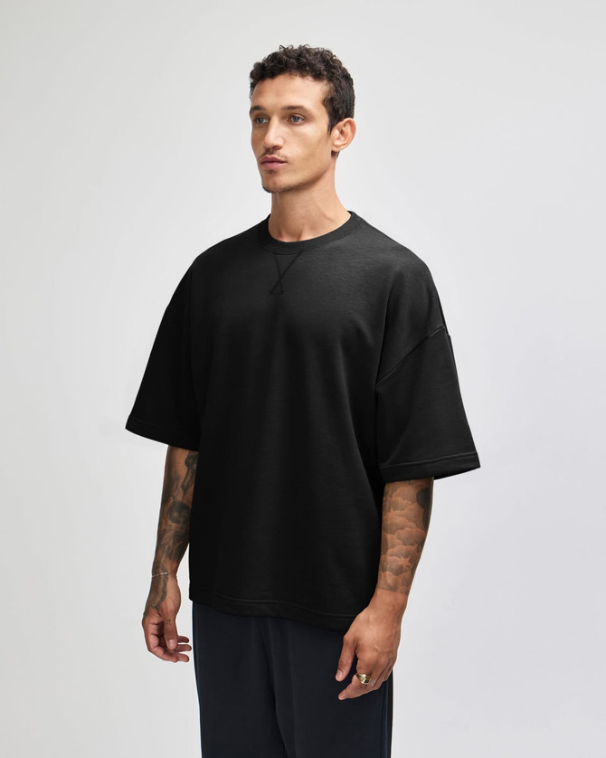 A black oversized boxy top with short sleeves displayed on a model from the side, featuring a logo.