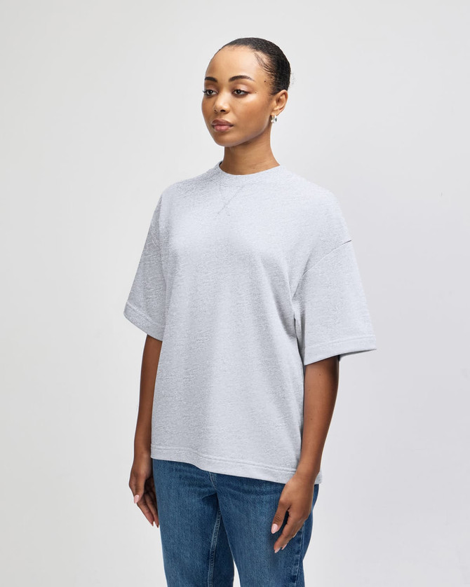 A grey oversized unisex boxy top displayed on a model, showcasing a side profile view. The top features a logo.