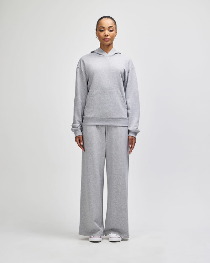 Grey wide-leg pants paired with a matching hoodie, featuring a logo, modelled by a standing woman.