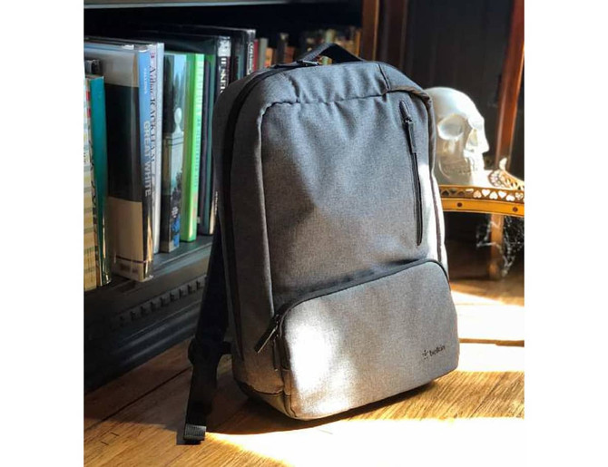 A grey backpack with multiple zippered compartments placed next to books and a decorative skull on a shelf.