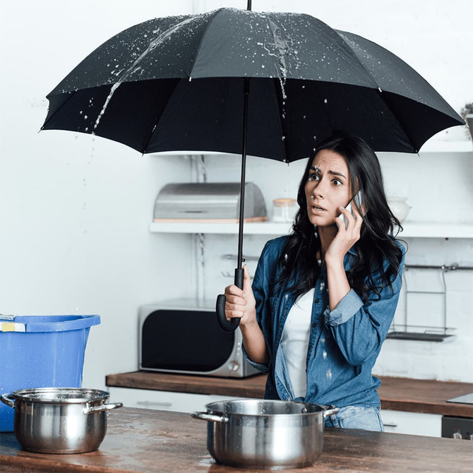 A black umbrella with water droplets is held by a woman, who appears concerned while on the phone in a kitchen setting.