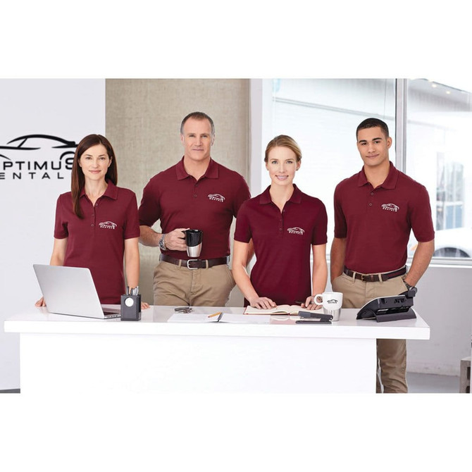 Four individuals are wearing maroon short sleeve polo shirts and are standing at a desk with various office items.