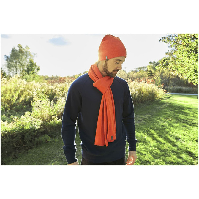 A man wearing an orange knit beanie and an orange scarf, standing in a green outdoor setting.