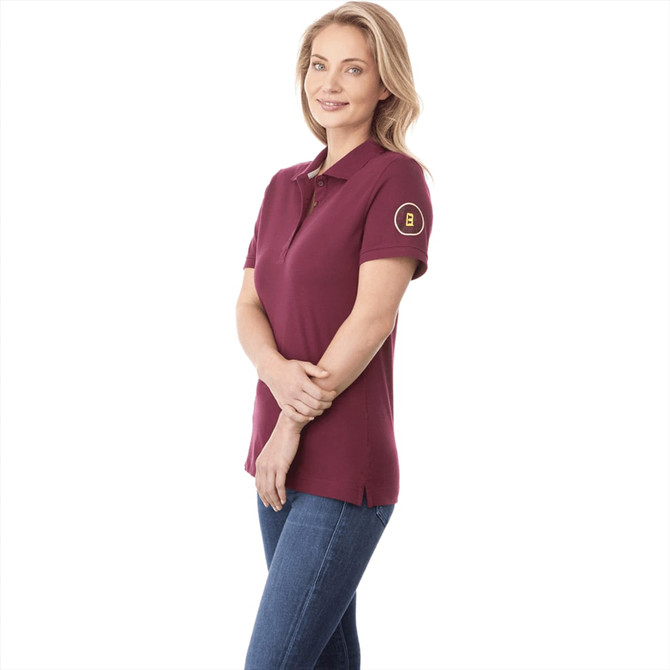 A maroon women's polo shirt with short sleeves and a logo on the sleeve, styled with jeans.