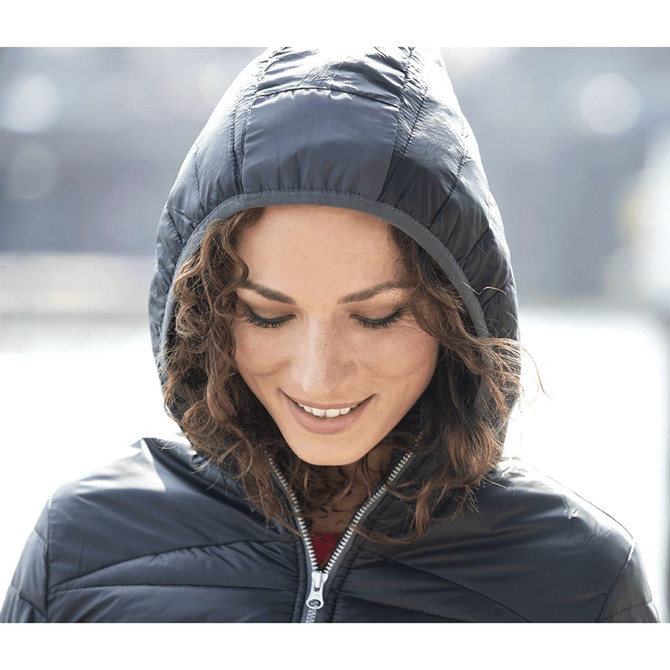 A woman wearing a navy insulated jacket with a hood, smiling gently in an outdoor setting.